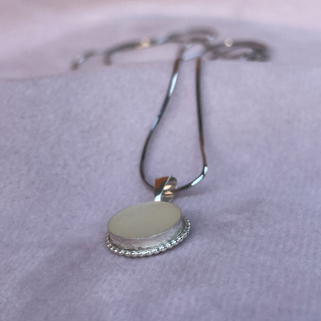 Deze borstmelk mamahanger heeft een sierlijke afgewerkte rand, met in de bezel eigen persoonlijke moedermelk